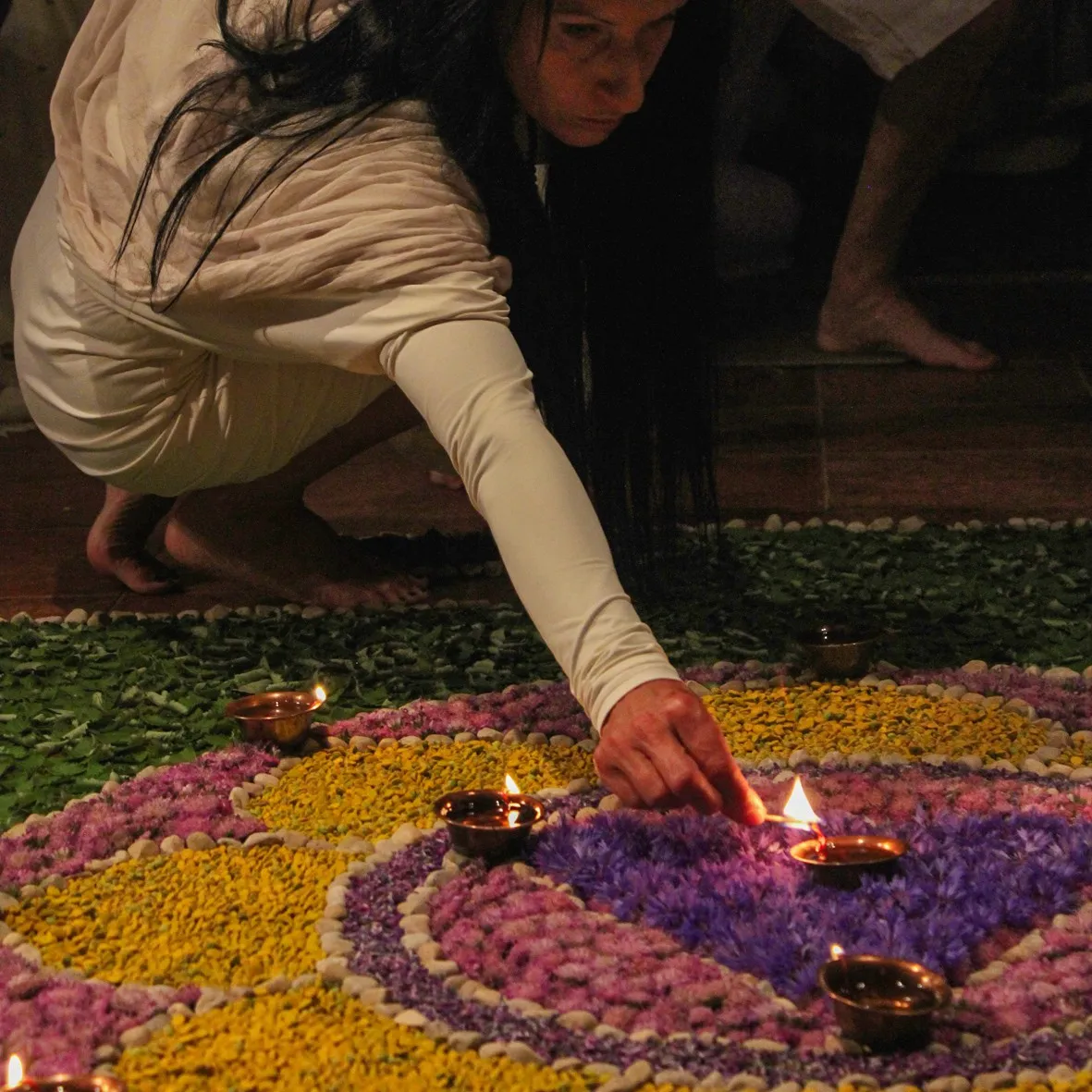 A woman lighting oil lamps in a mandala of flowers