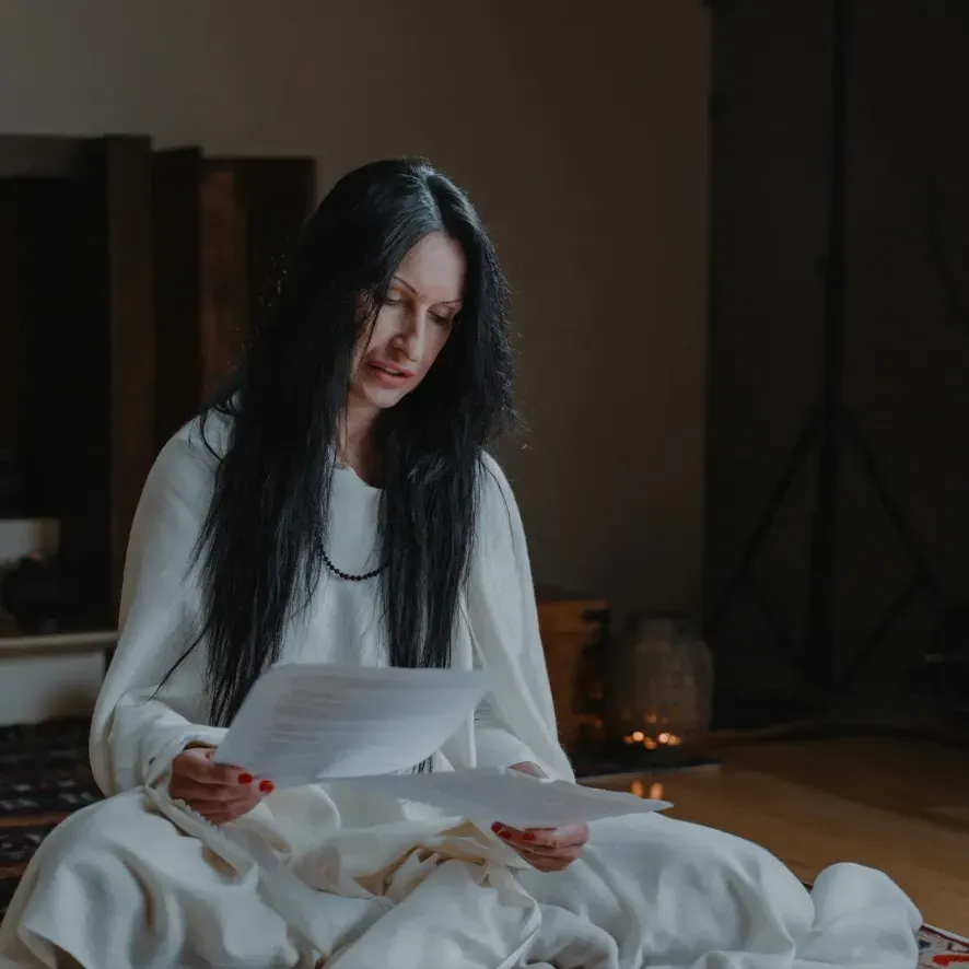A woman in white sitting on the floor, reading from sheets of paper